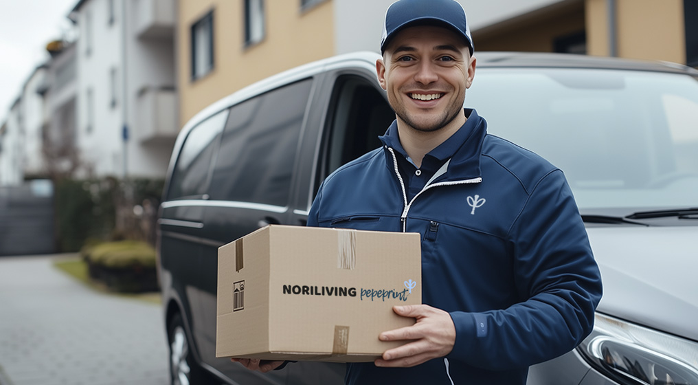 Ein Lieferbote in blauer Uniform hält ein Paket vor einem Lieferwagen in einer Wohngegend.